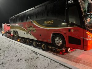 Front-side view of a coach bus on a lowboy trailer at night.