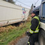 Worker in high-visibility clothing beside a truck at the roadside.