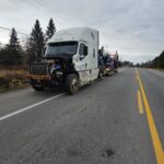 White truck with its engine exposed at the front and recovery vehicles behind it.
